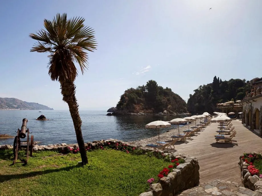 Spiaggia privata con lettini, ombrelloni, palma e vecchio cannone affacciata sulla baia