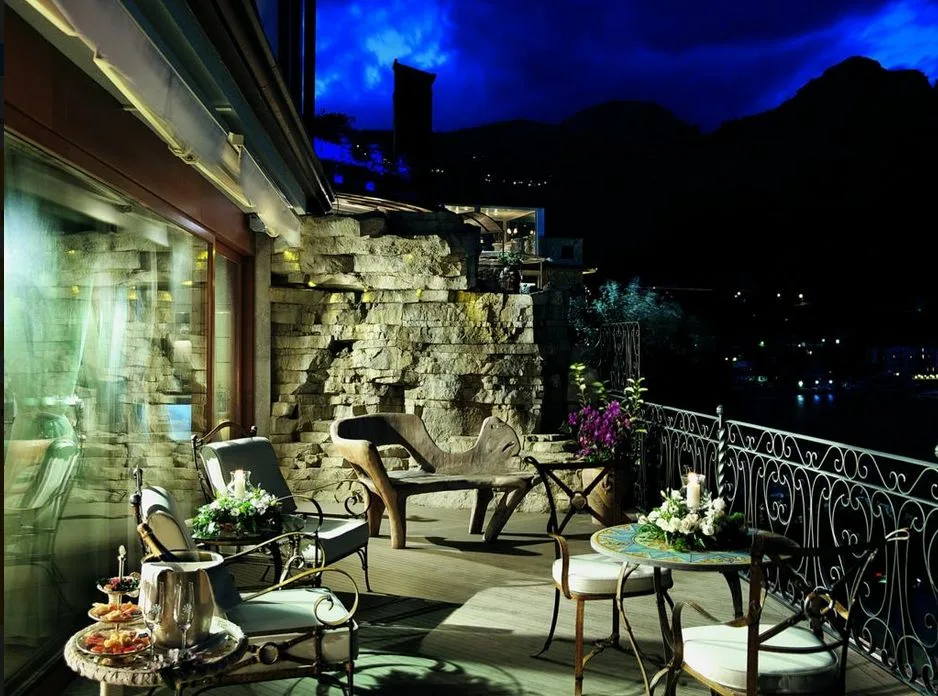 Terrazza serale con parete in pietra, poltrone e vista notturna sul mare e le montagne