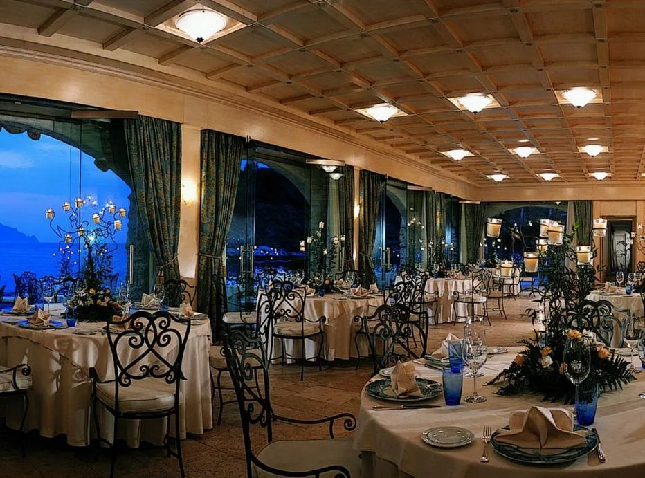 Sala ristorante interna serale con tavoli apparecchiati e ampie vetrate sul mare