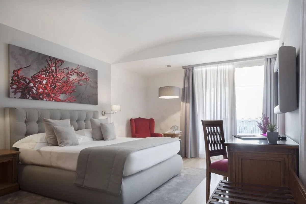 Camera luminosa con letto matrimoniale, poltrona rossa e opera d'arte a corallo