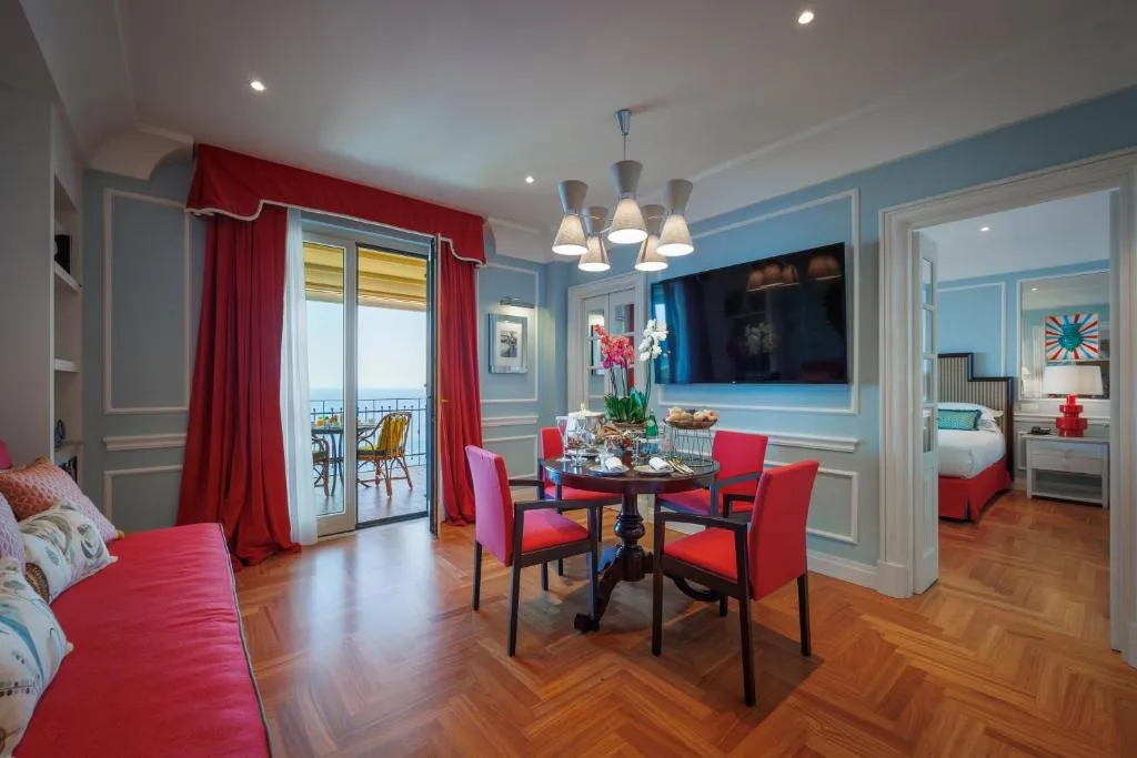 Soggiorno della suite con zona pranzo, divano rosso e balcone vista mare